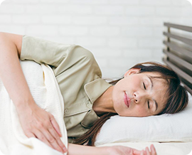 生活習慣の見直しのイメージ｜白いベッドの上で静かに眠る若い女性の横顔。白いリネンのベッドカバーと明るい寝室で、質の良い睡眠と規則正しい生活習慣を表現